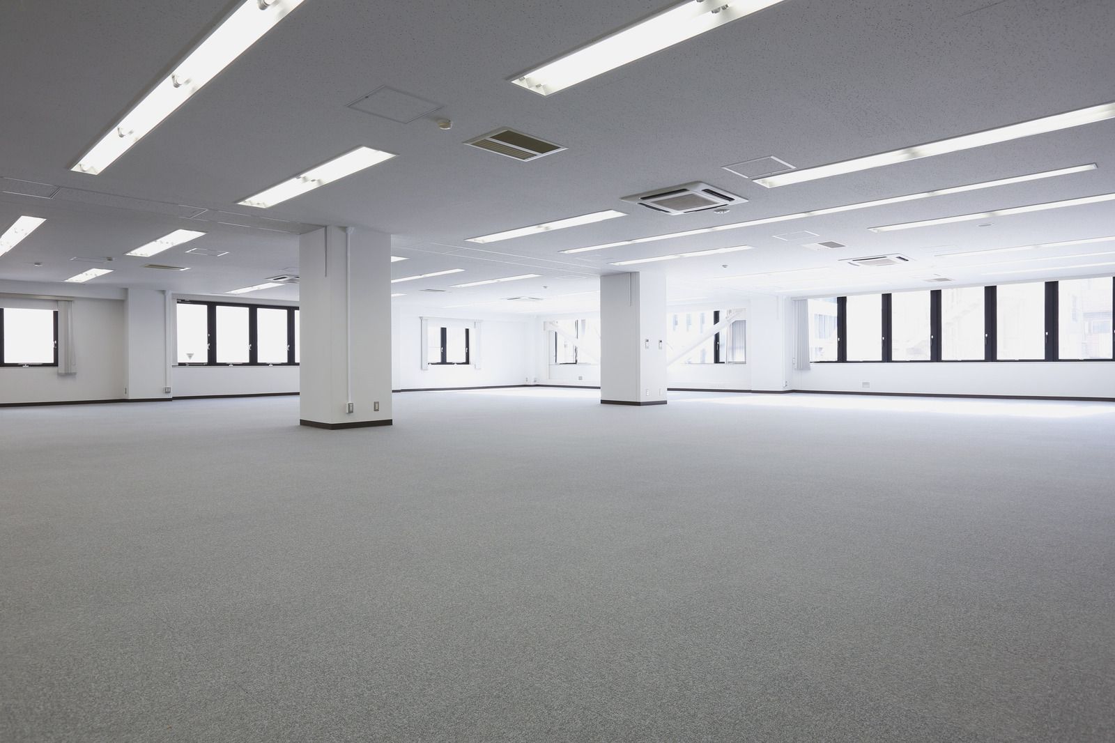 Empty, bright office space with white columns, fluorescent lights, and gray carpet.
