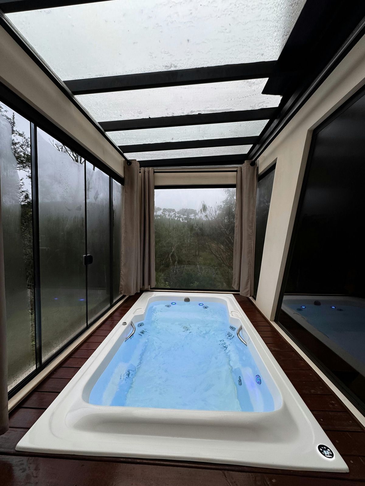 Indoor spa with blue water, surrounded by glass walls and a skylight roof.