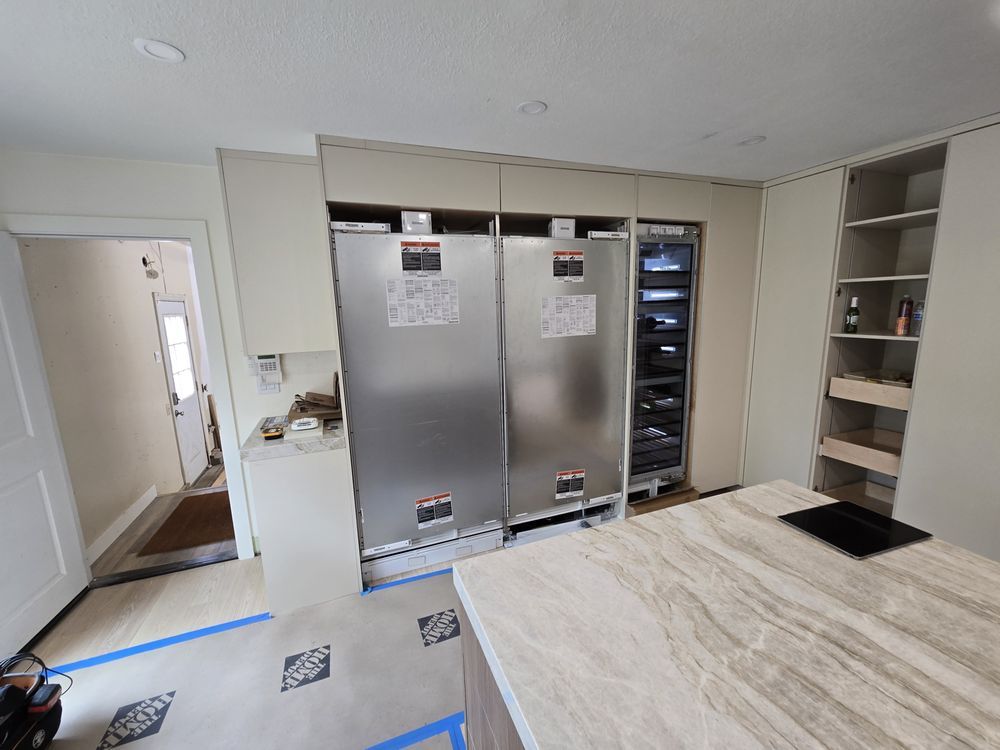Kitchen with large stainless steel refrigerators, wine cooler, and built-in shelving, under construction.