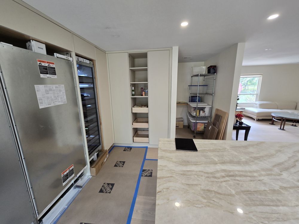 Kitchen with refrigerator, pantry, and island, undergoing renovation. Blue tape protects the floor.