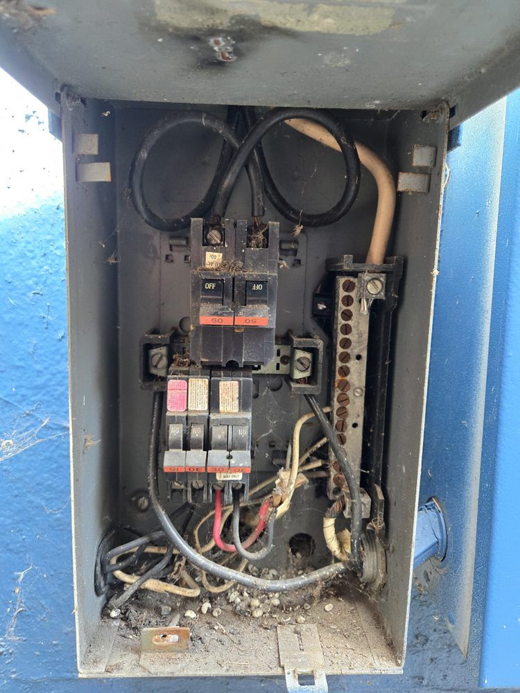 Open electrical panel with circuit breakers, wires, and a grounding bar; interior view.