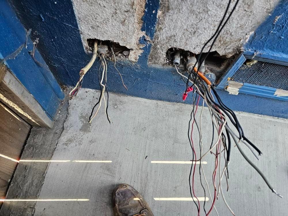 Exposed electrical wires protrude from ceiling holes above a concrete floor. A foot is in the lower part of the frame.