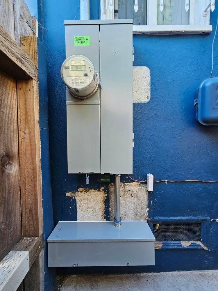 Electrical meter and panel on a blue exterior wall with a utility box below.