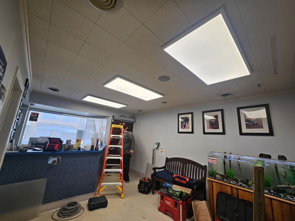Person on ladder working on ceiling lights in an office.  Includes bench, fish tanks, and tools.