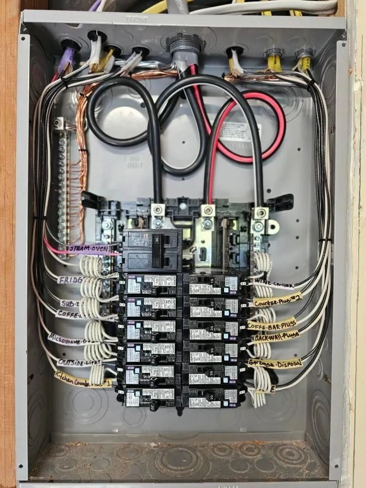 Electrical panel with wires and circuit breakers. Gray metal box, wires labeled, black and white cables.