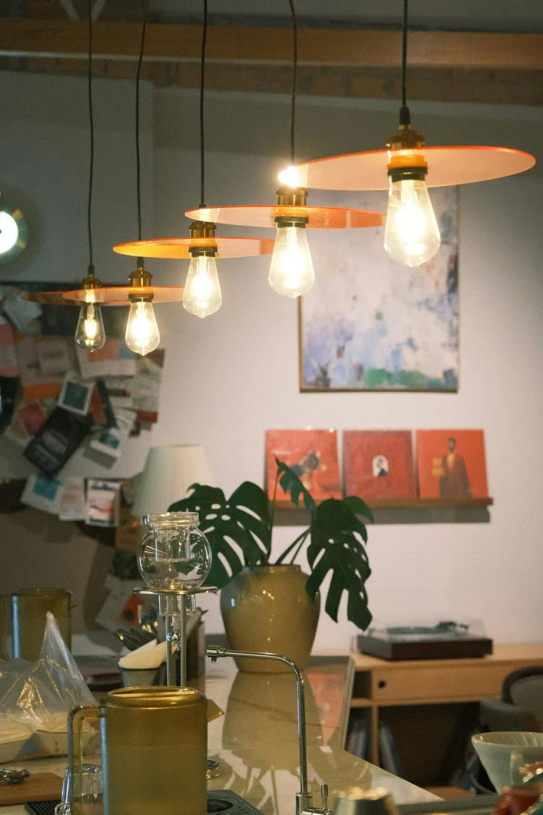 Row of pendant lights with orange shades, over a table with plants, art, and decor.