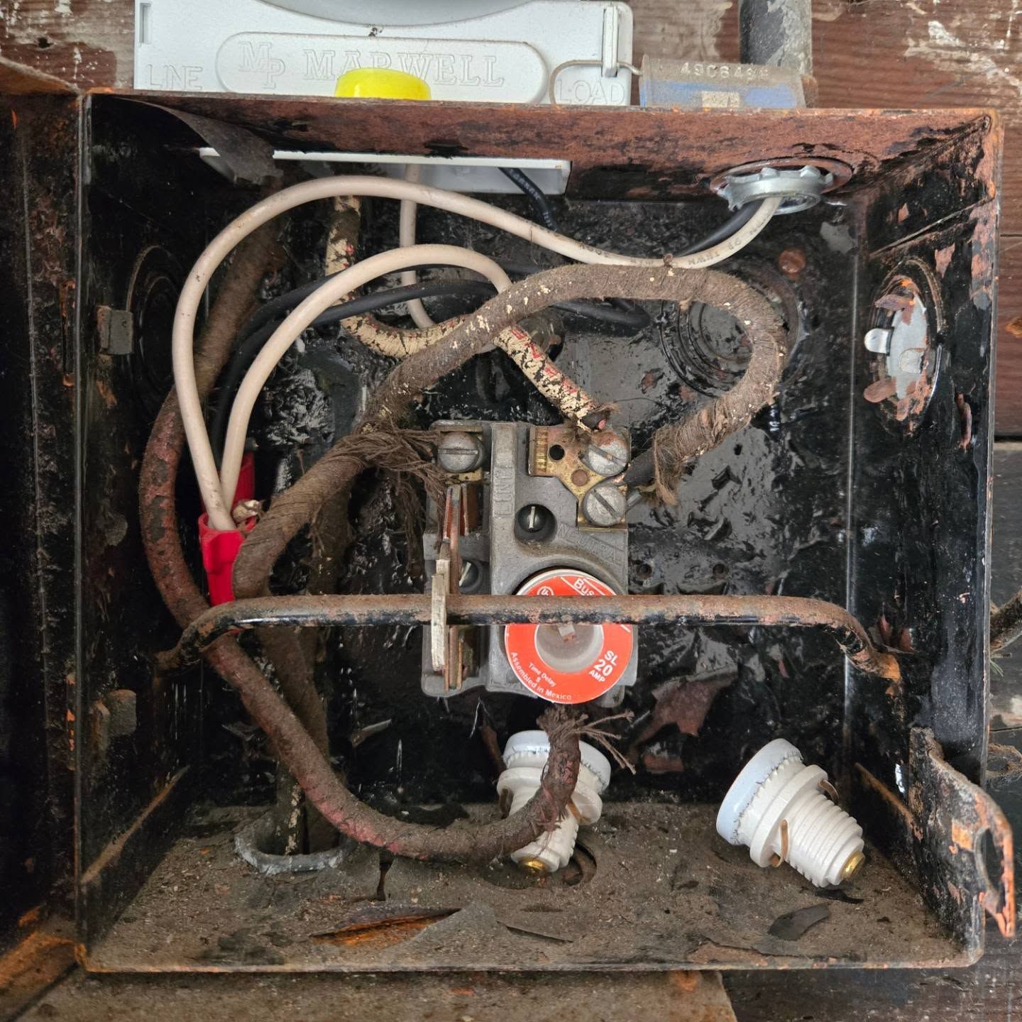 Open, rusted electrical box with wires, a fuse, and light sockets.