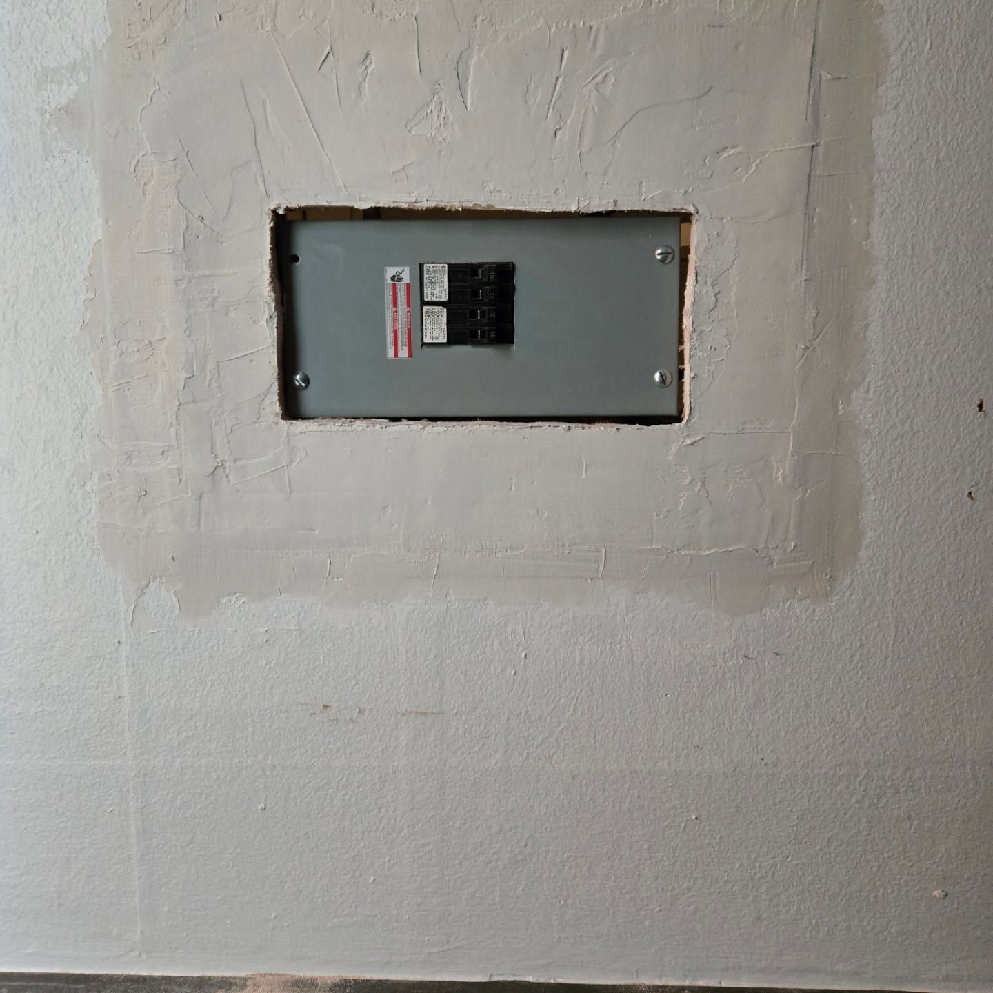 Electrical panel recessed in a light-colored wall, surrounded by fresh plaster.