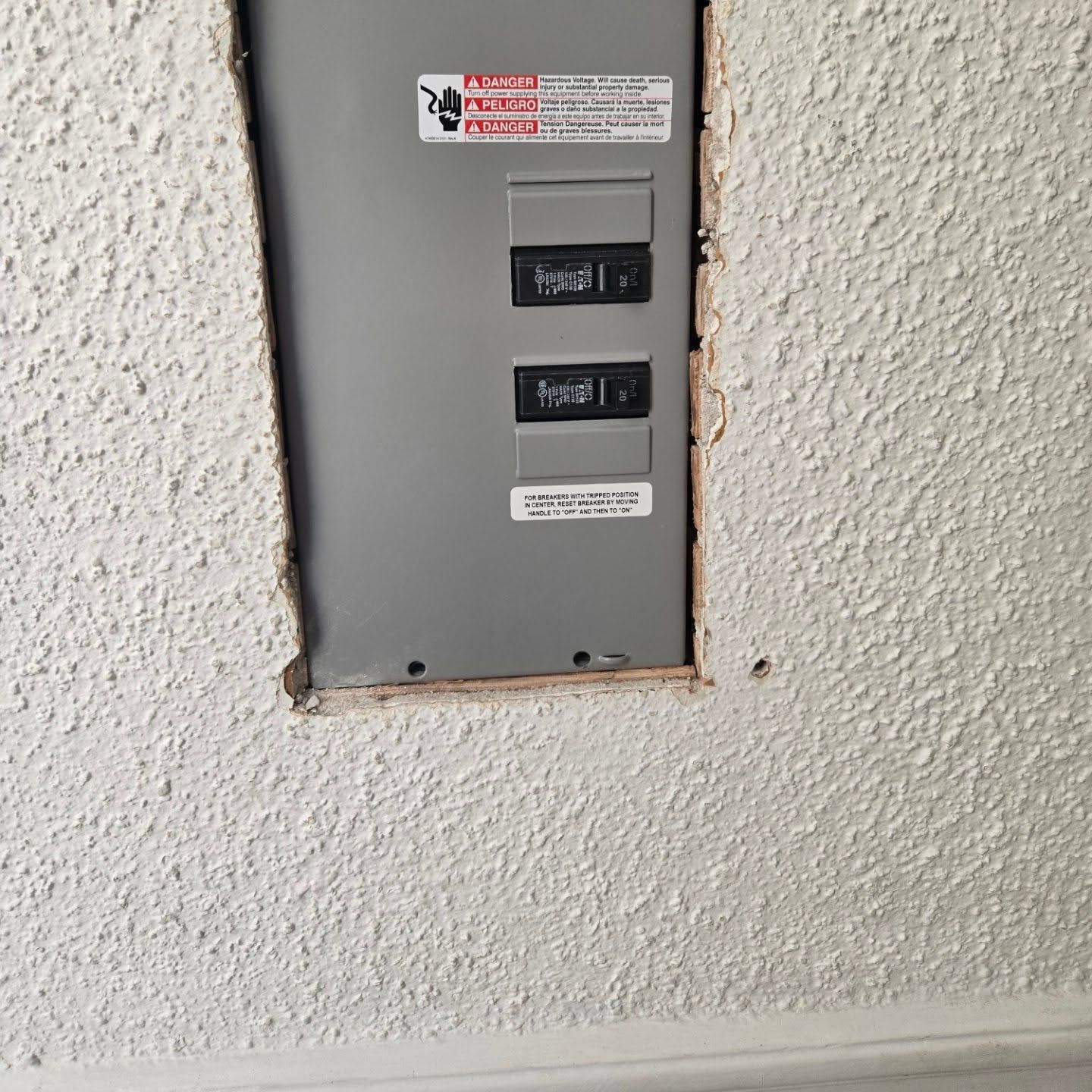 Electrical panel recessed in textured white wall; two circuit breakers visible.