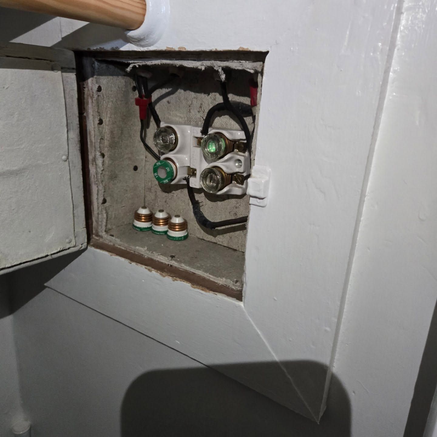 Open electrical panel with fuses and wiring, inside a white painted box.