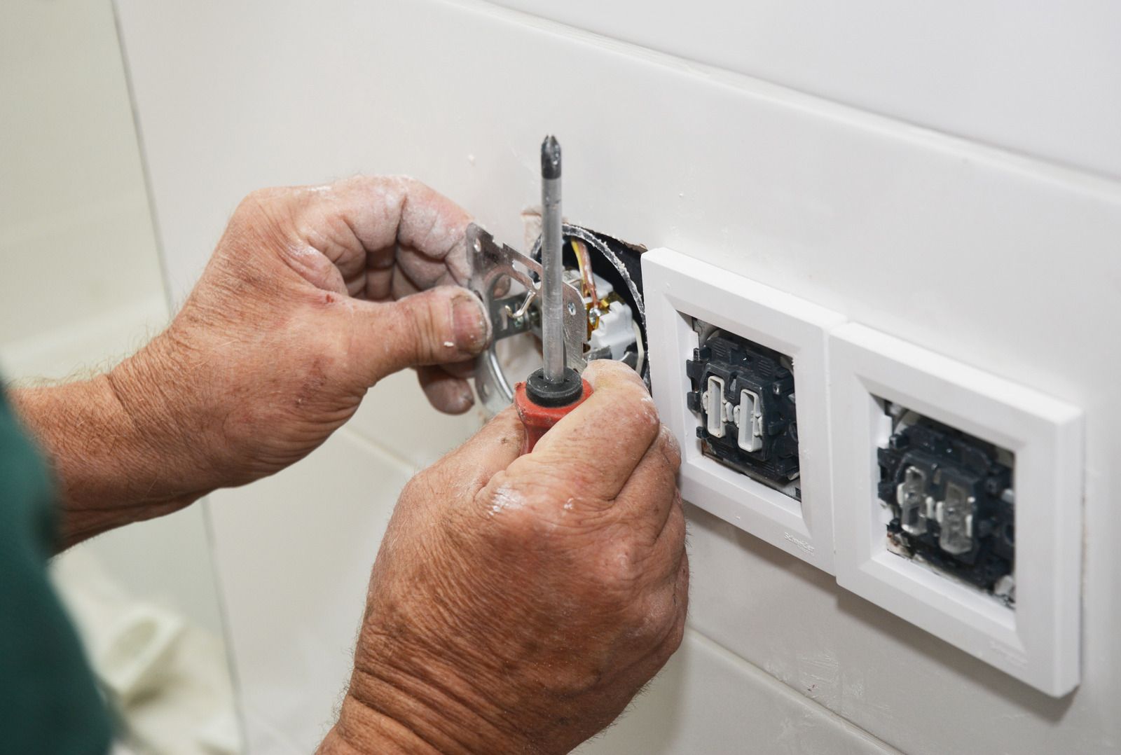 Hands of a person using a screwdriver to install an electrical outlet.