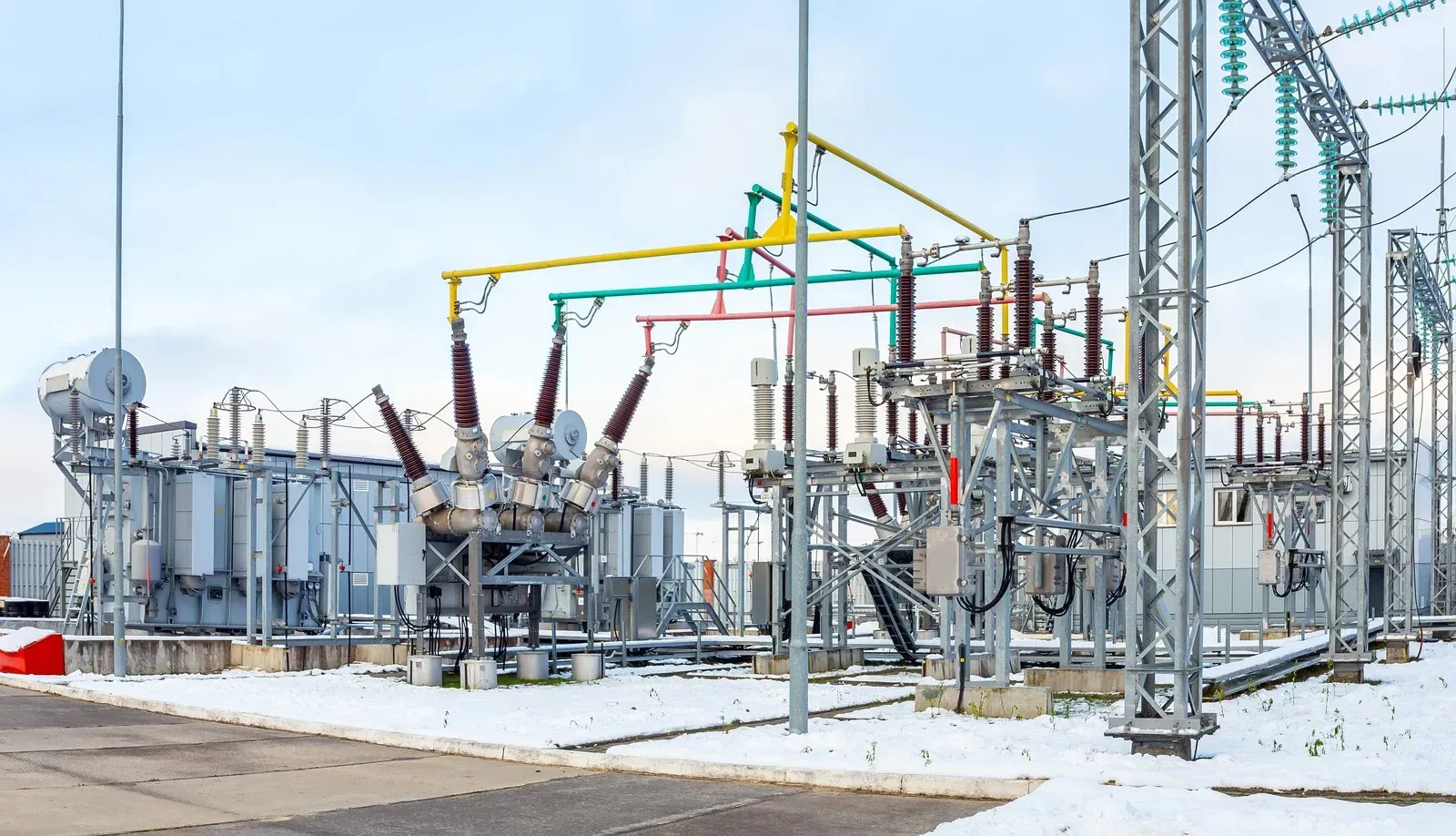 Electrical substation with transformers, insulators, and power lines in a snowy environment.