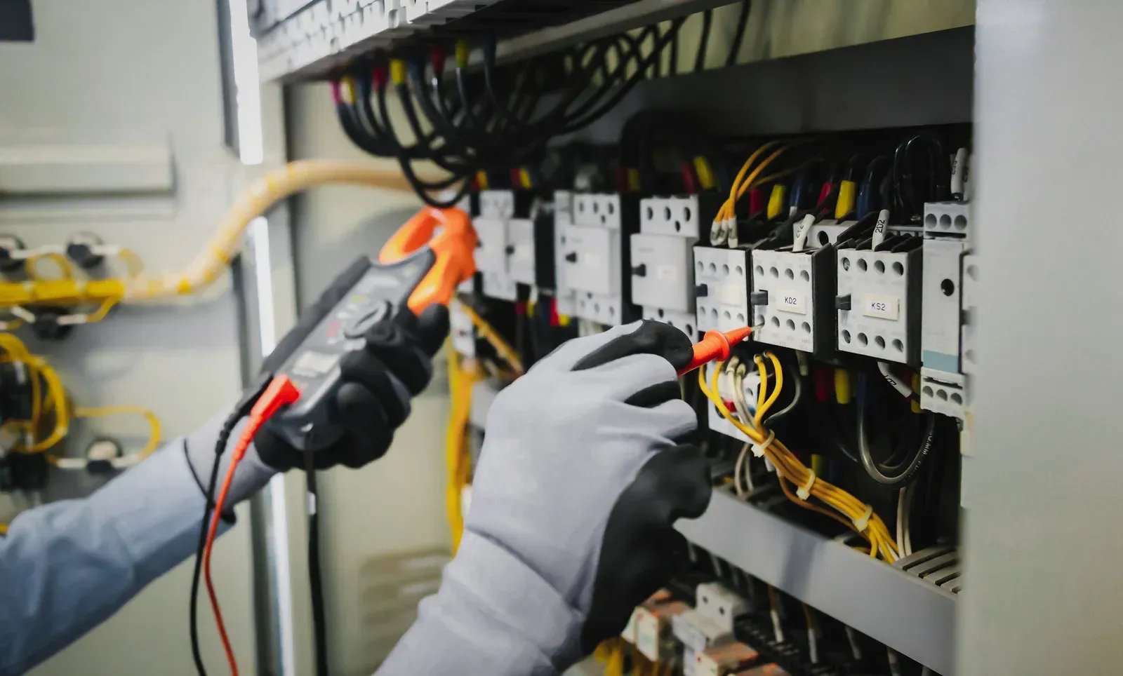 Electrician wearing gloves tests electrical panel with multimeter.