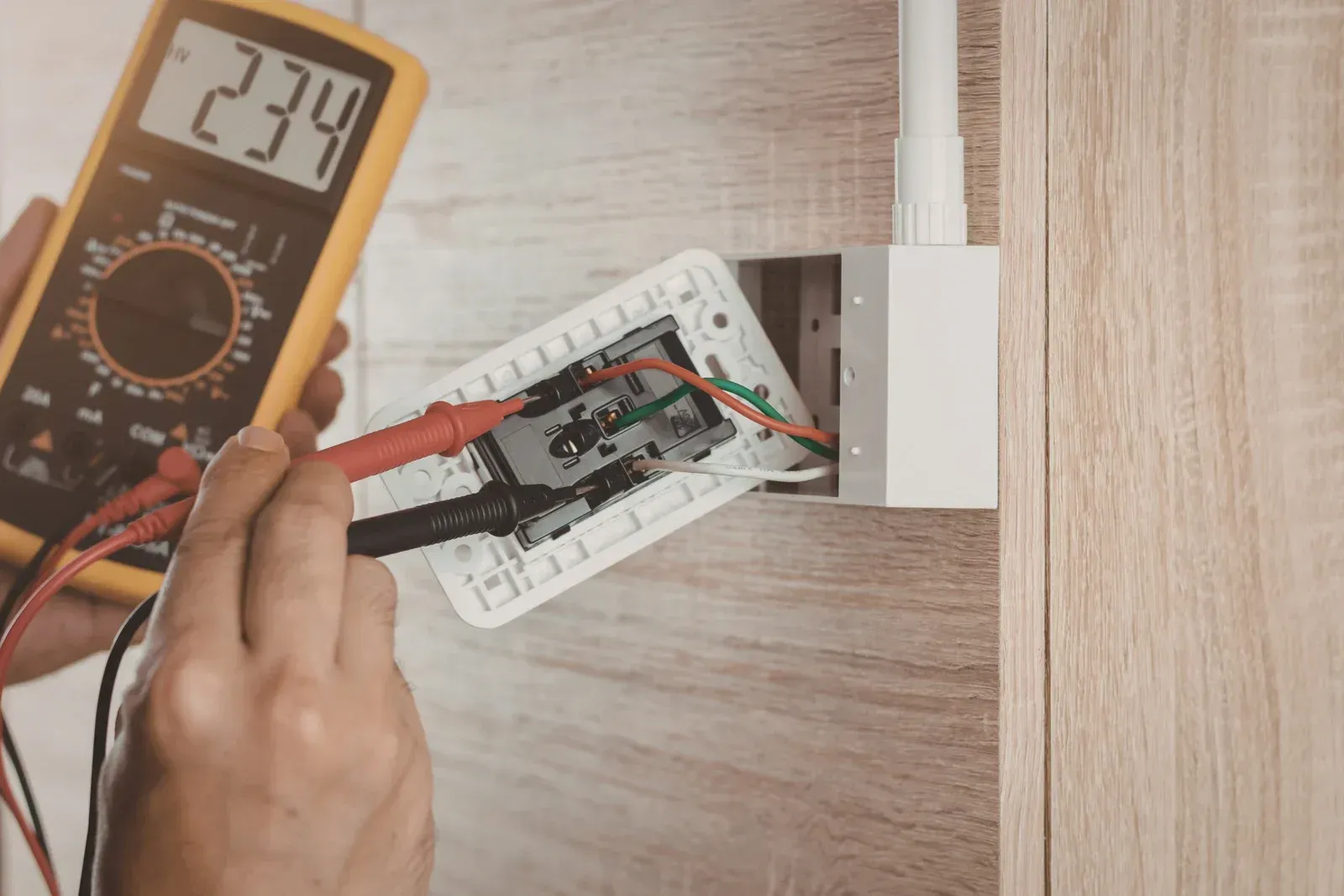 Hand testing electrical outlet with a multimeter, displaying 234 volts.