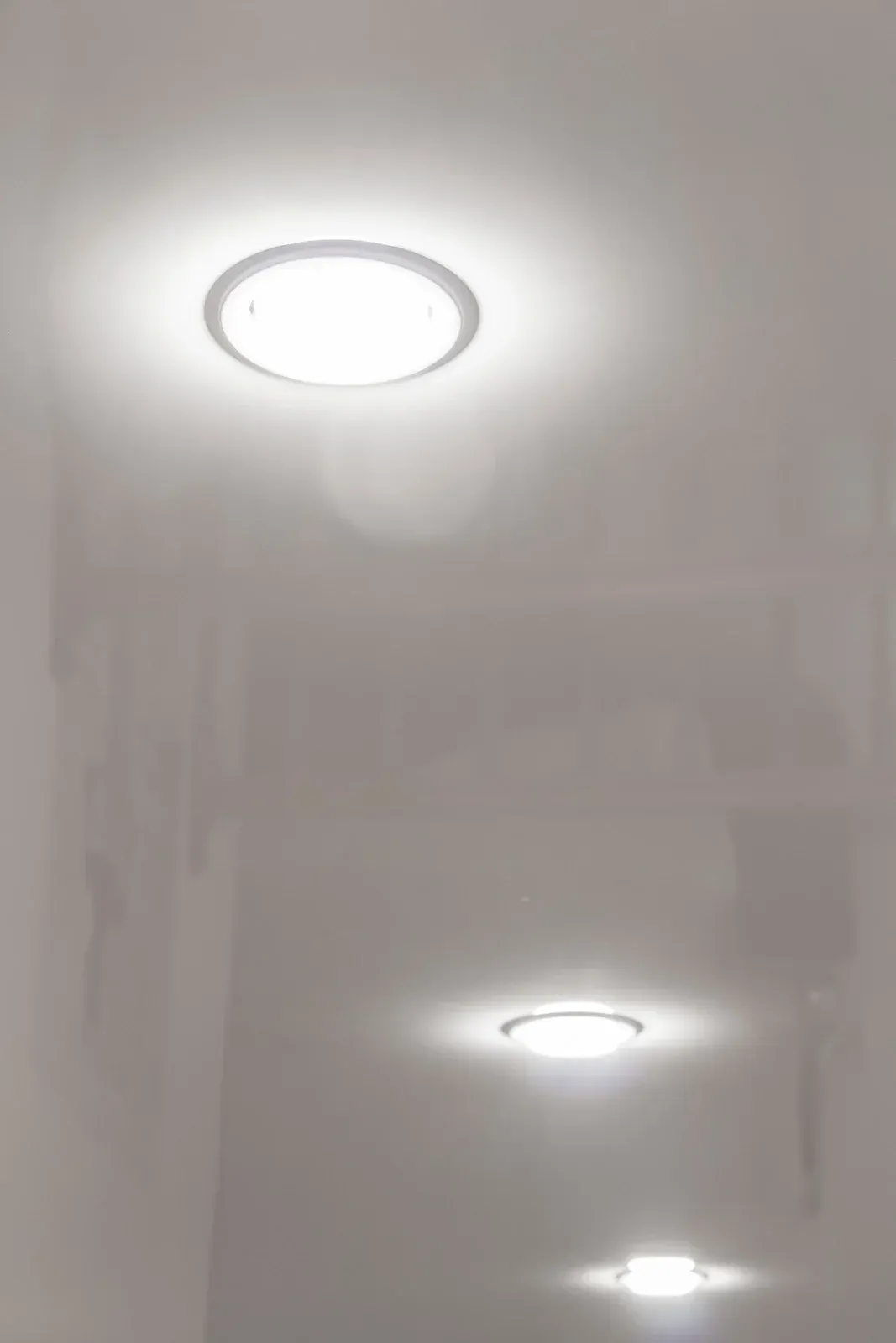 Three round, recessed ceiling lights illuminate a white hallway.