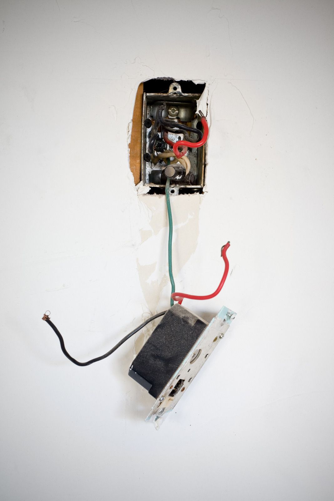 Electrical wires spilling out of an unfinished wall outlet on a green and white wall.