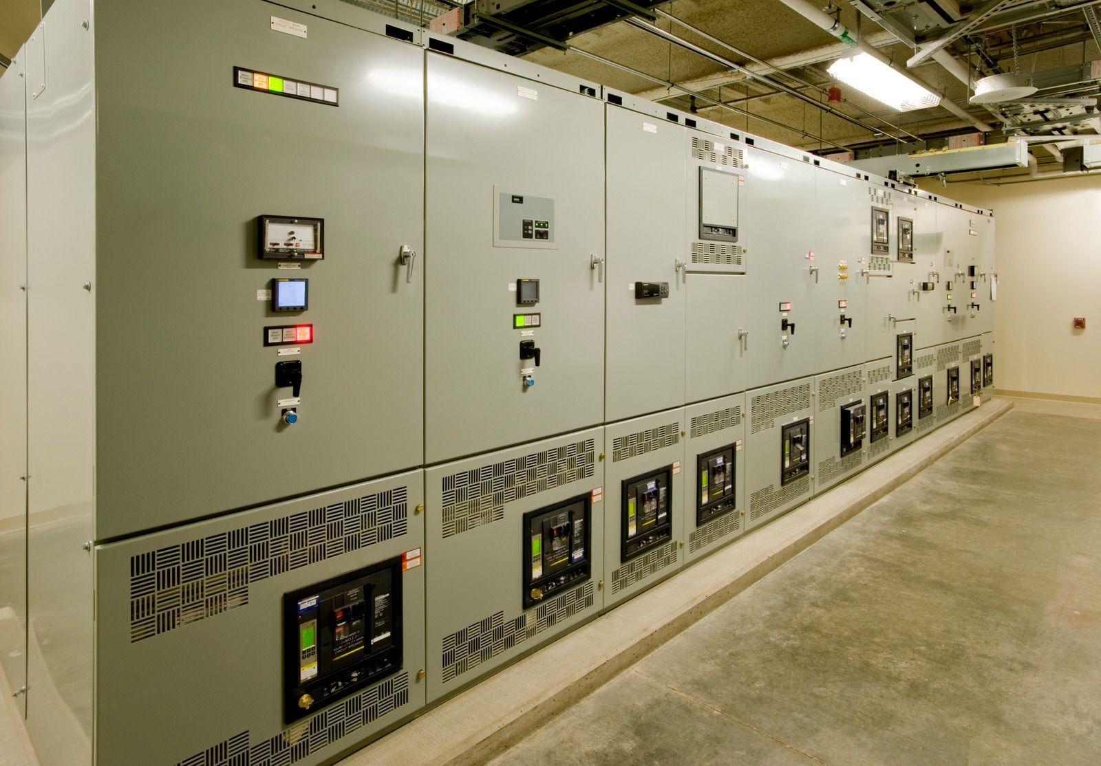 Electrical switchgear in a utility room; gray cabinets with various dials, gauges, and controls.