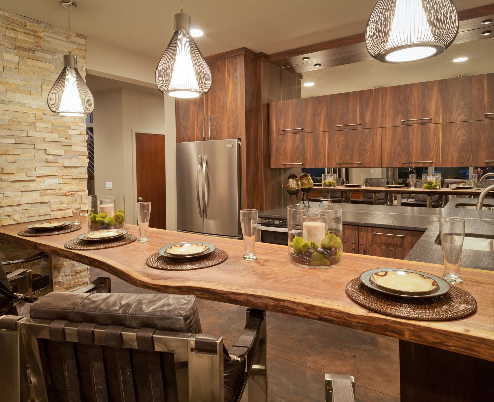 Modern kitchen with live-edge wooden bar, pendant lights, stainless steel appliances, and wood cabinets.