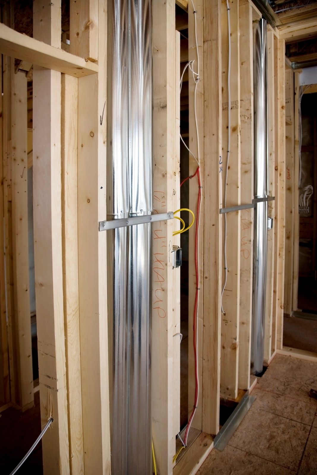 Wooden wall studs with vertical metal ductwork, and electrical wiring.