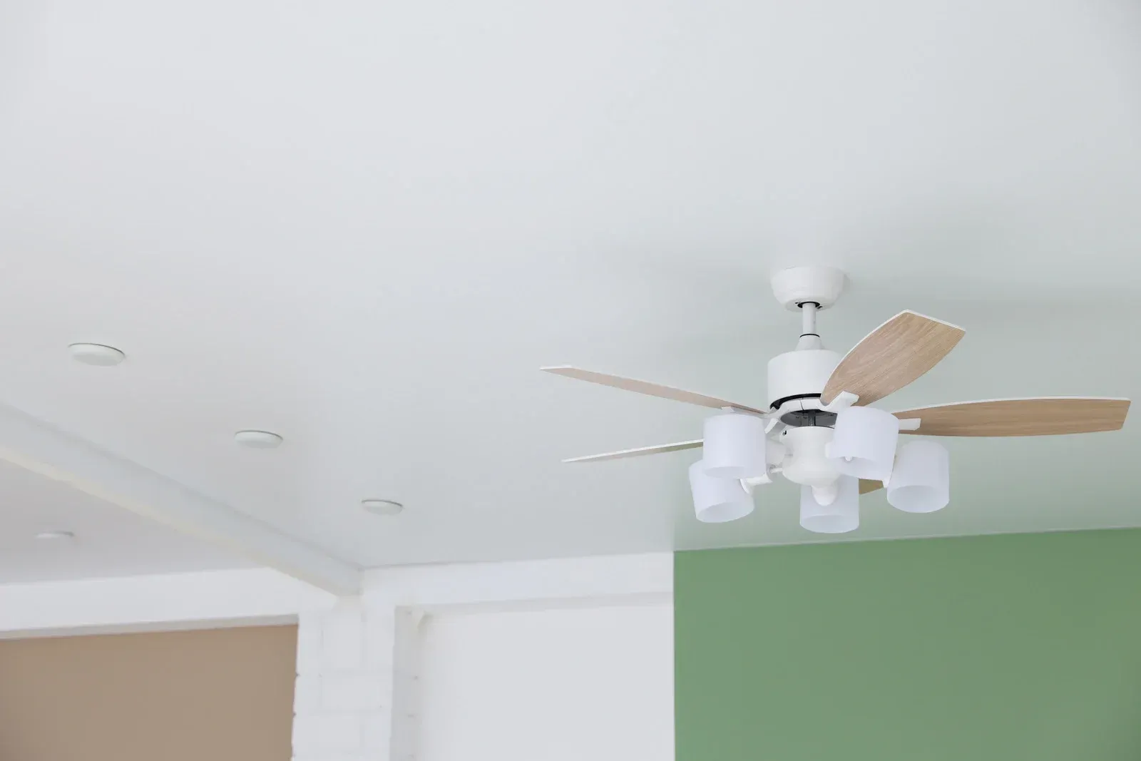 Ceiling fan with light fixtures on white ceiling, next to green wall.