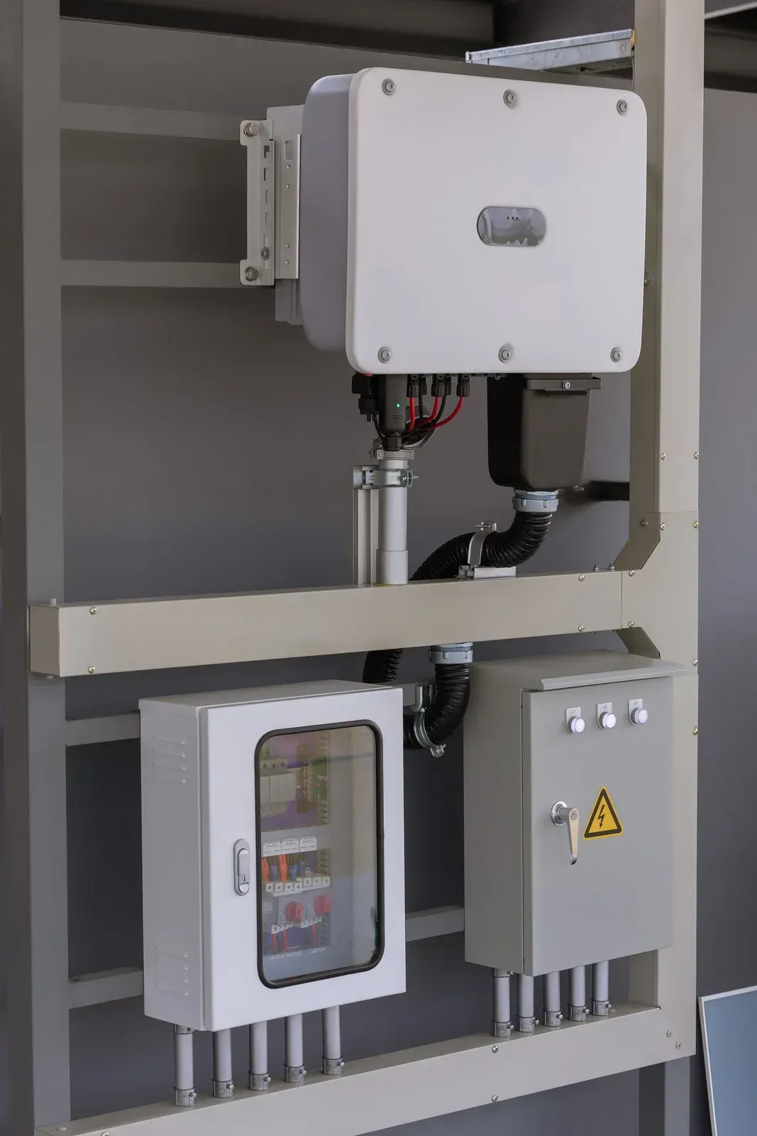 Solar panel equipment mounted on a grey metal frame. Includes an inverter, electrical boxes, and conduits.