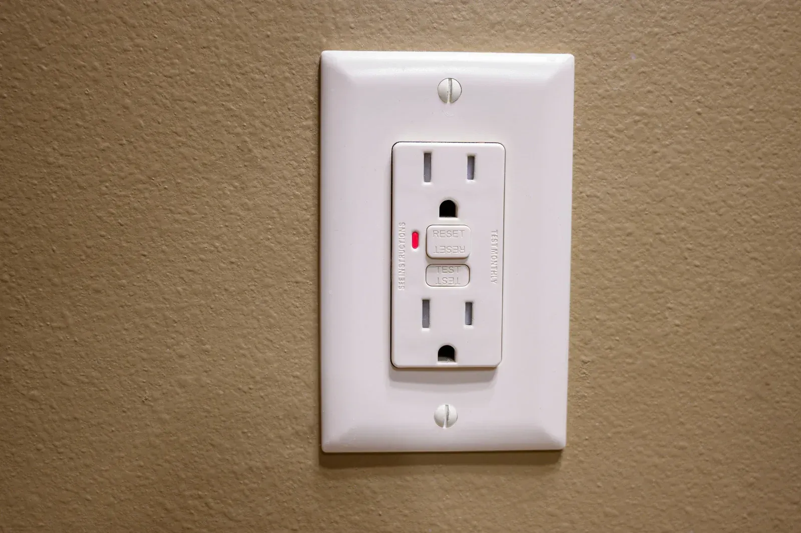 White GFCI outlet on beige wall.  Has a test and reset button.