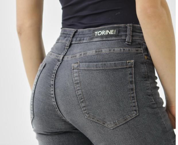 Mujer con vaqueros grises, vista trasera. Vaqueros de cintura alta con etiqueta de la marca.