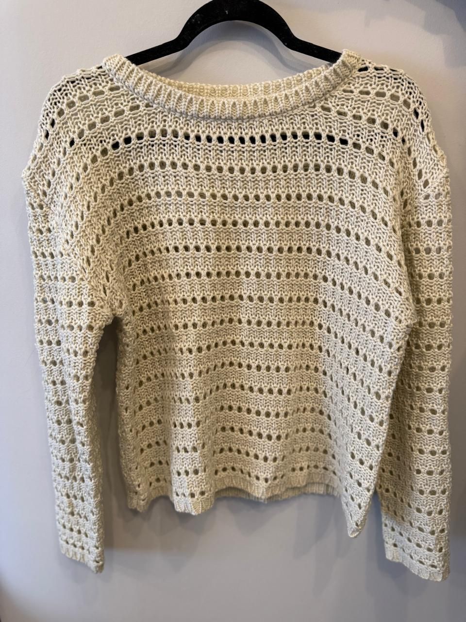 Suéter de punto abierto de color crema en percha negra.