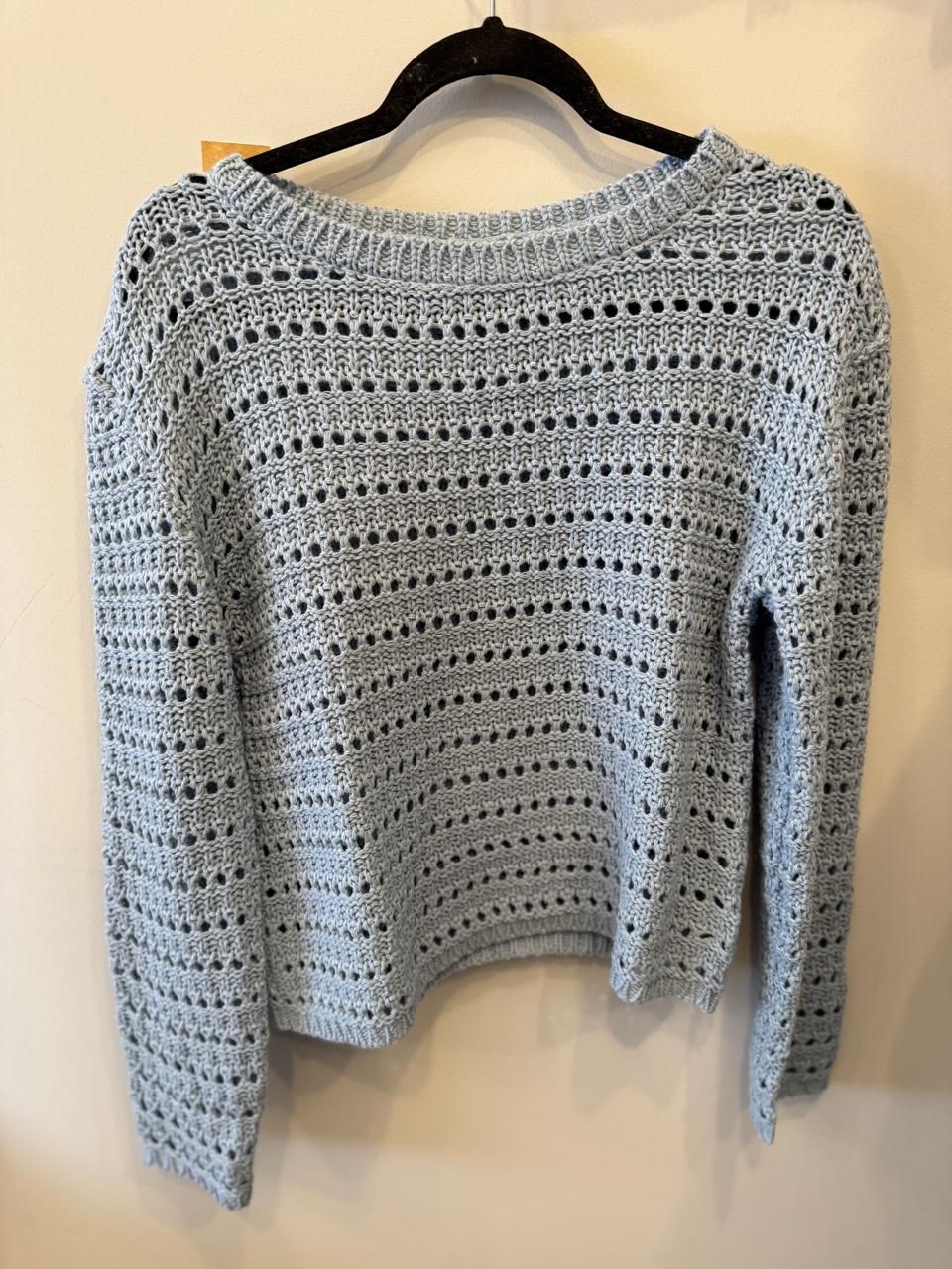 Suéter de punto abierto de color crema en percha negra.