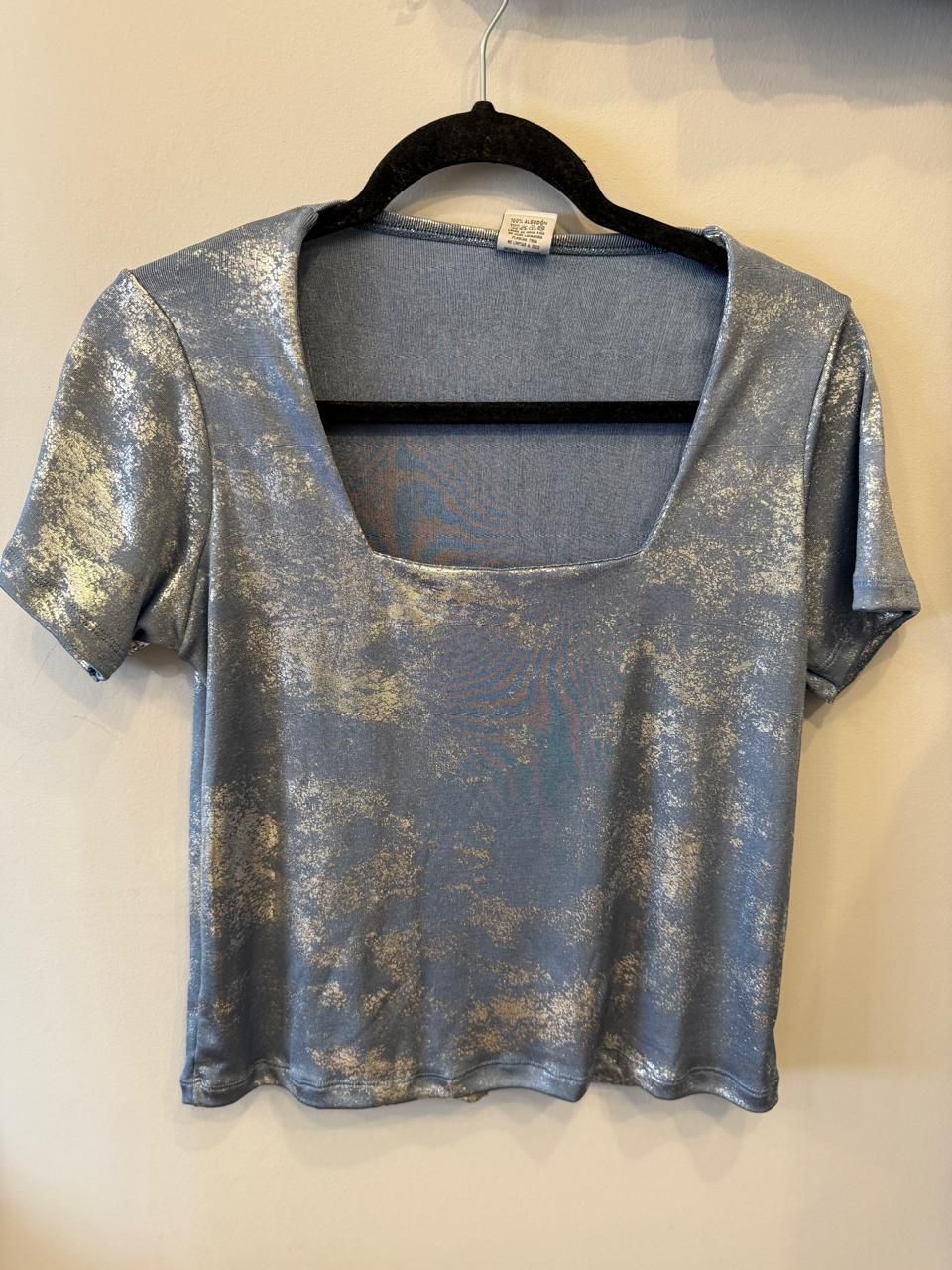 Top corto blanco con estampado de salpicaduras grises, escote cuadrado, colgado en percha negra.