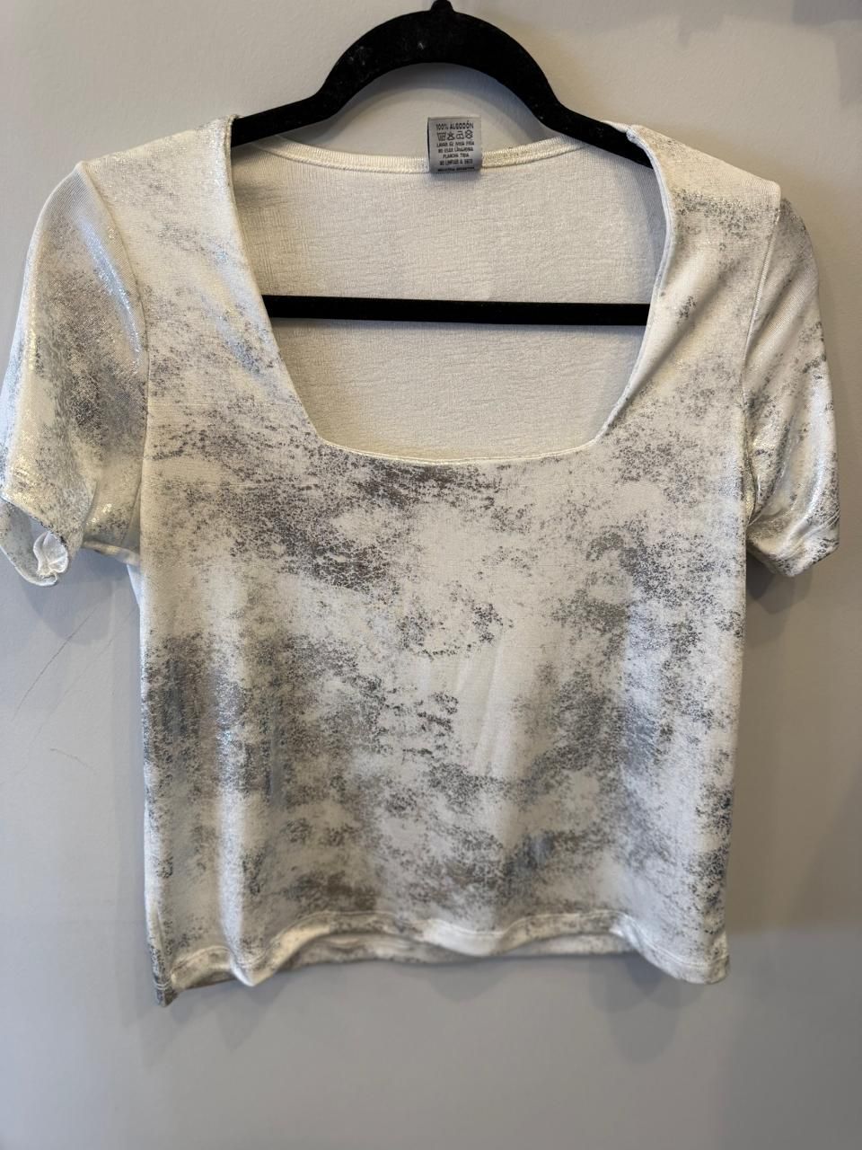 Top corto blanco con estampado de salpicaduras grises, escote cuadrado, colgado en percha negra.