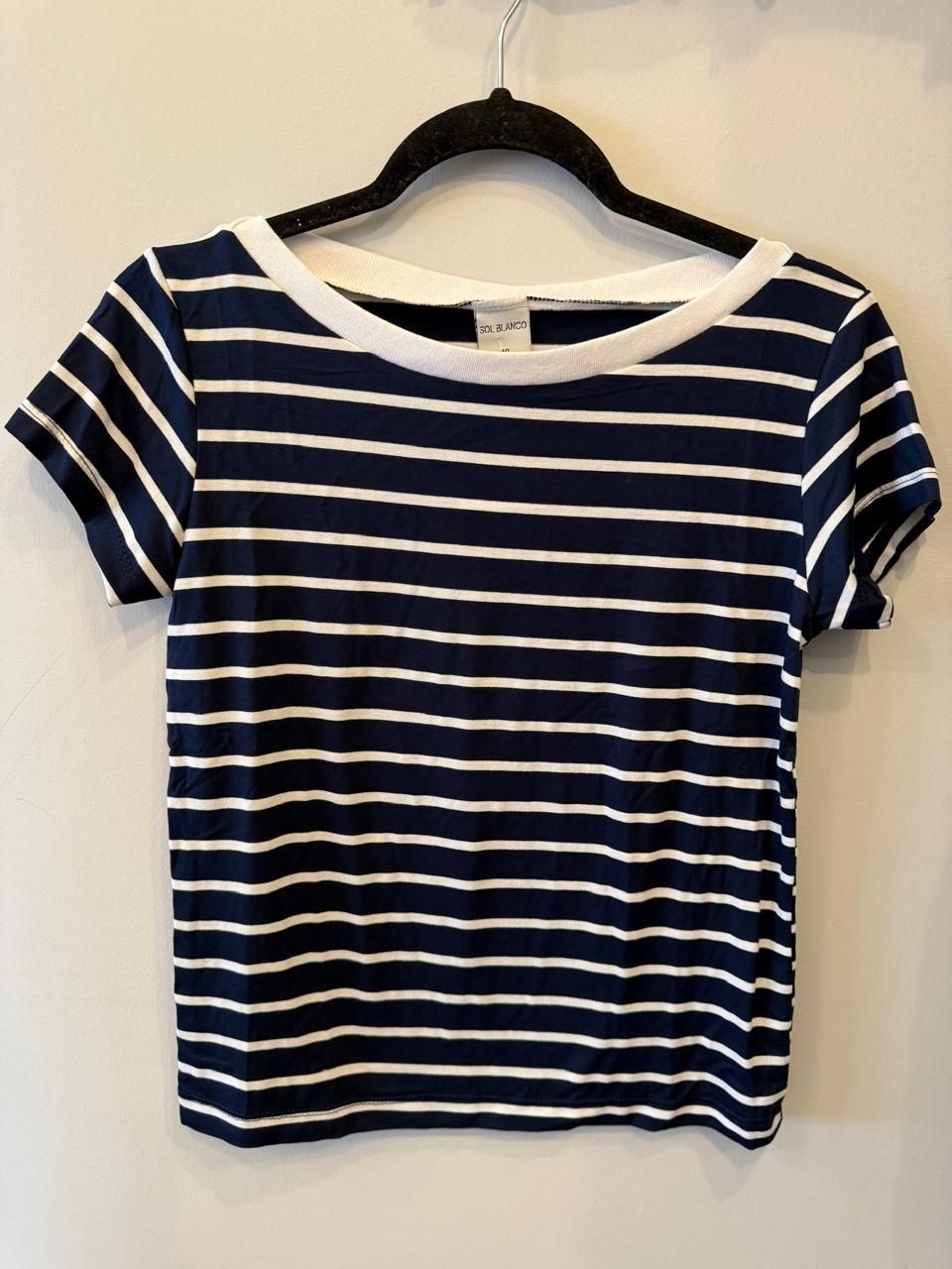 Camiseta de rayas azul marino y blancas, con cuello blanco y manga corta, colgada en una percha negra.