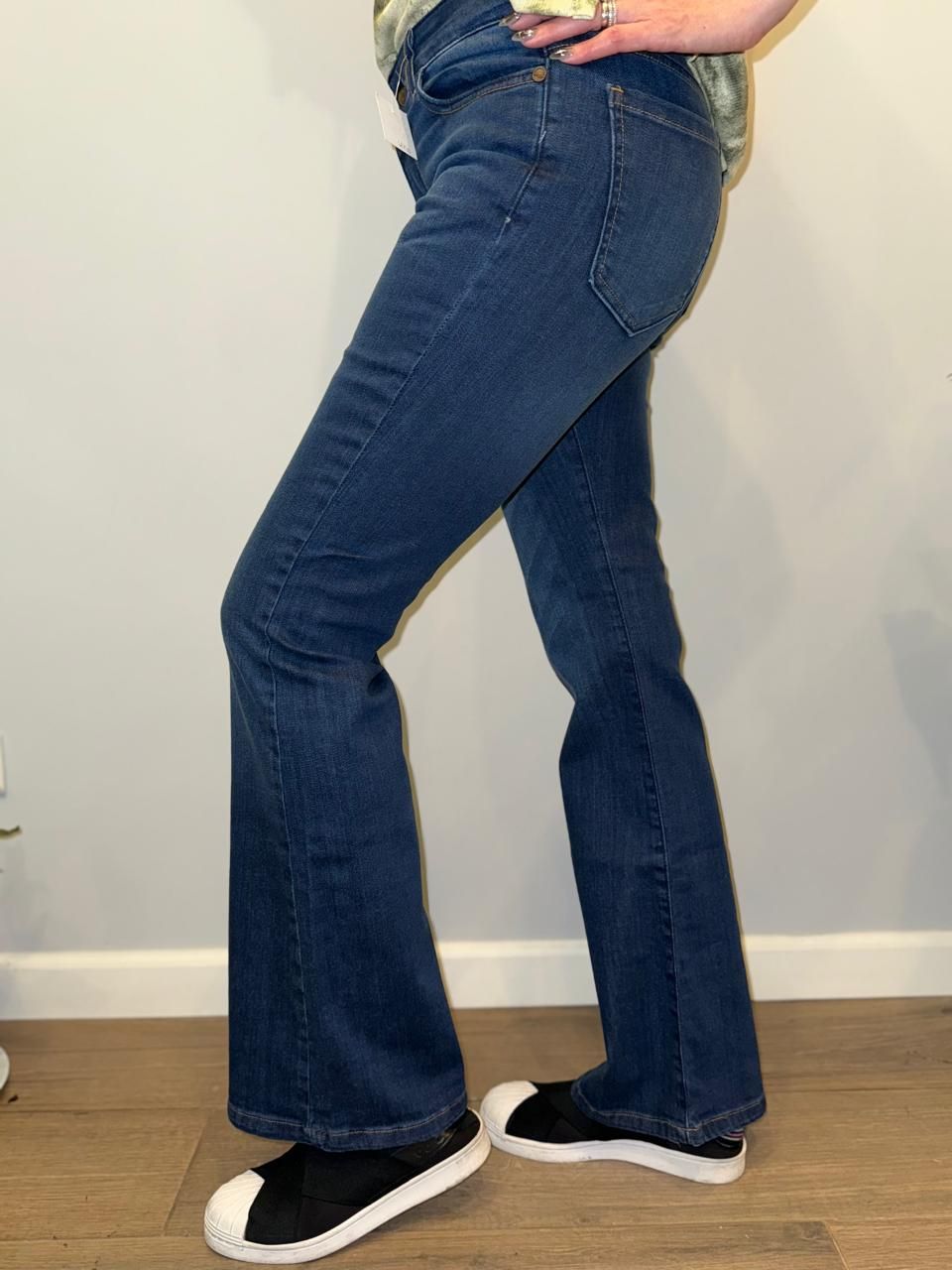 Mujer que lleva pantalones vaqueros acampanados de color azul oscuro con zapatillas blancas y negras.