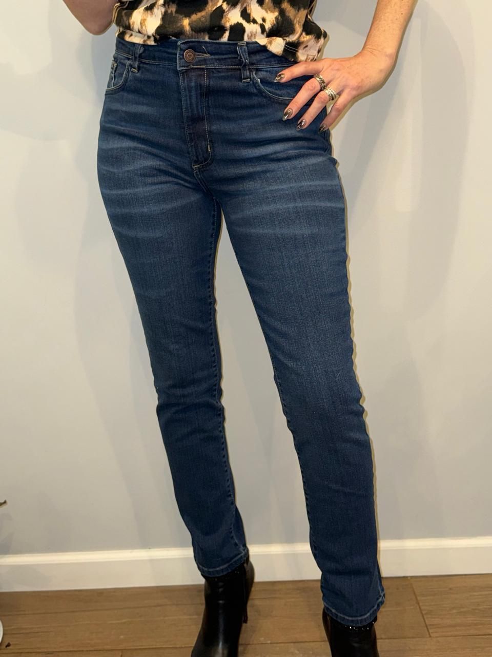 Persona con vaqueros oscuros de cintura alta y botas negras. De pie en un interior.