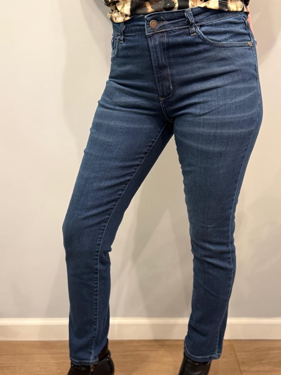 Persona con vaqueros oscuros de cintura alta y botas negras. De pie en un interior.