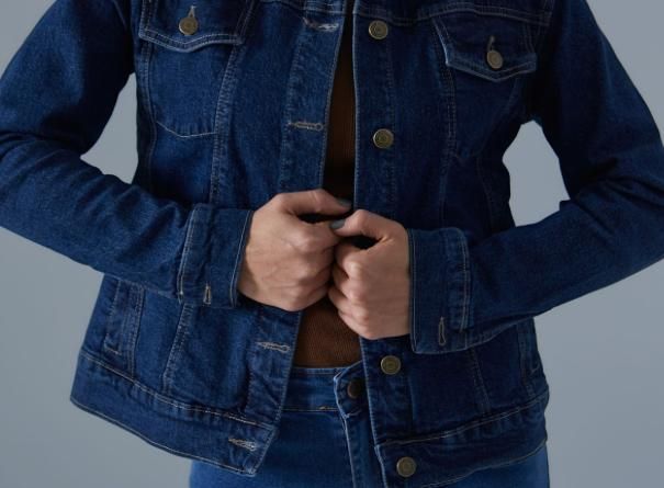 Persona con chaqueta vaquera azul oscuro, con las manos cerca del pecho, a punto de abotonarse.