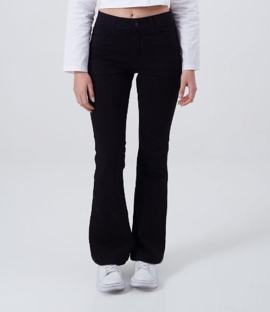 Pantalones acampanados negros y zapatillas blancas en las piernas de una persona, vista lateral, sobre un fondo blanco.