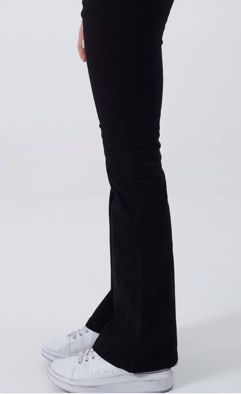 Pantalones acampanados negros y zapatillas blancas en las piernas de una persona, vista lateral, sobre un fondo blanco.