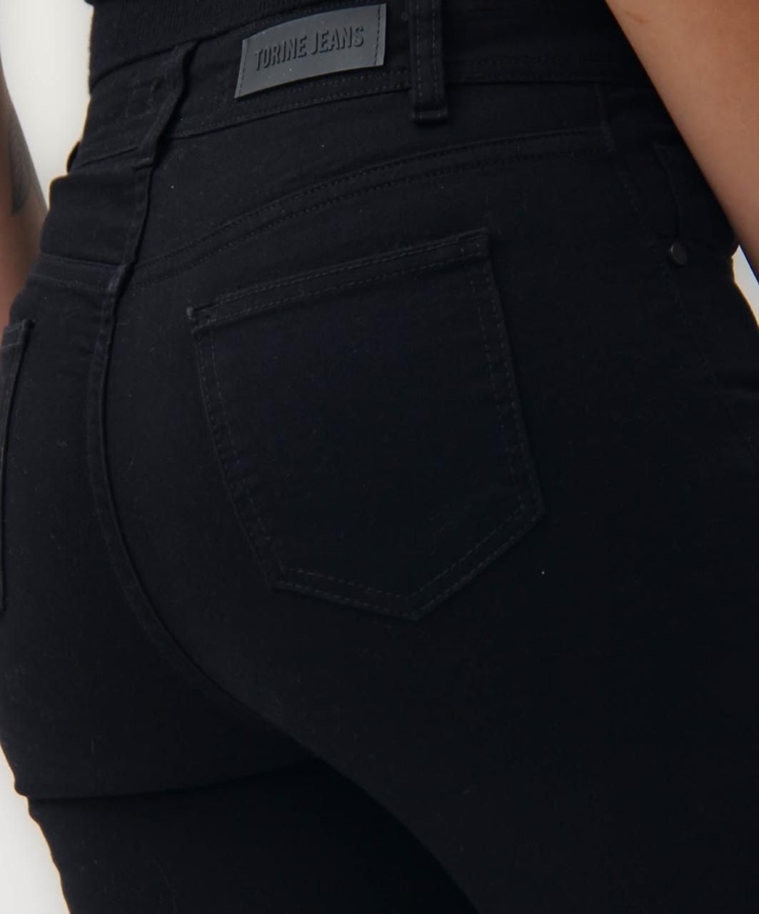 Mujer que viste jeans negros y zapatillas de deporte, de pie sobre un fondo blanco, subiendo la cintura de los jeans.