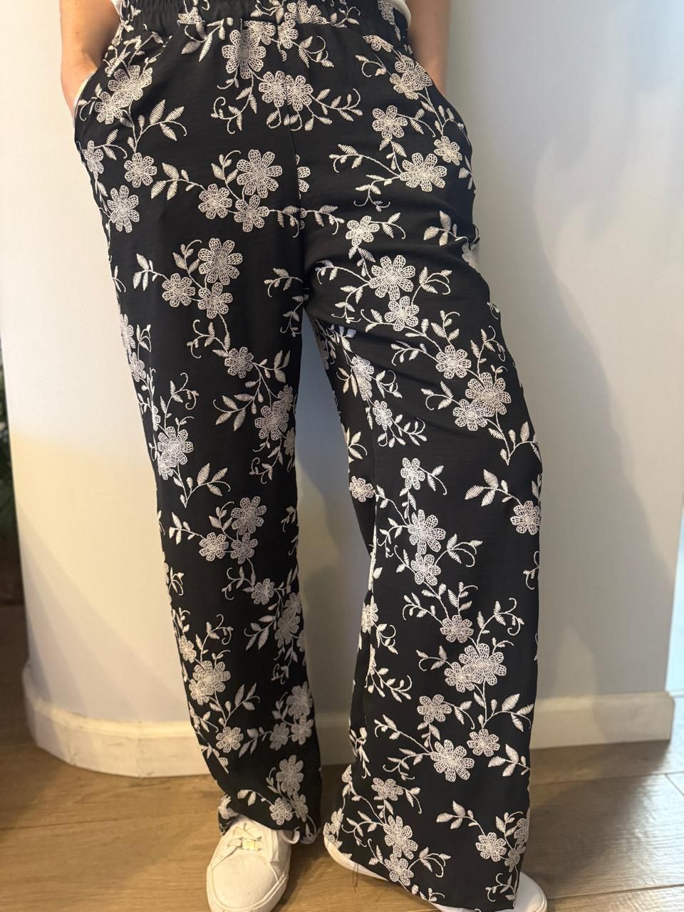 Pantalón negro con estampado floral, zapatillas blancas.