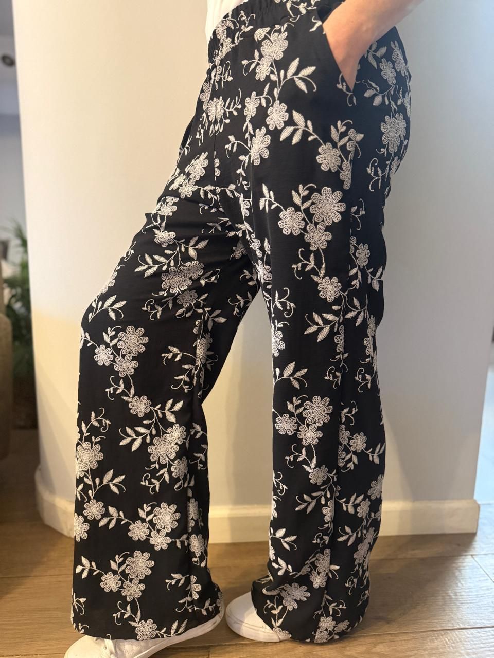 Pantalón negro con estampado floral, zapatillas blancas.