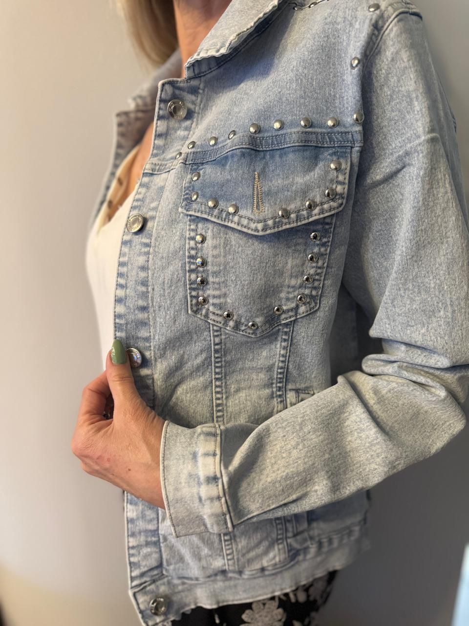 Mujer con una chaqueta vaquera azul claro con tachuelas plateadas, de pie y sosteniendo la chaqueta cerrada.