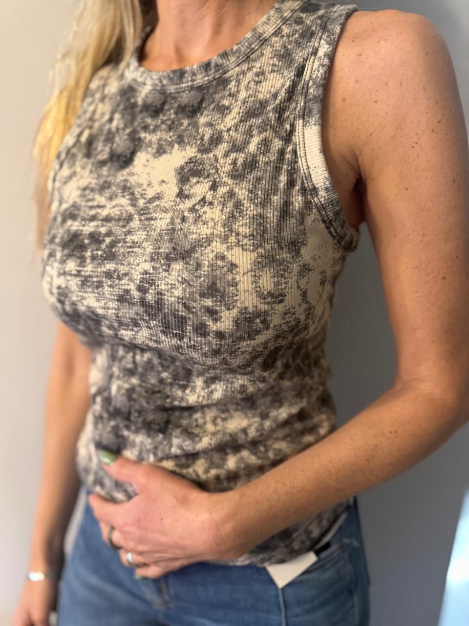 Mujer con una camiseta de tirantes acanalada con estampado tie-dye. Tira del bajo de la camisa.