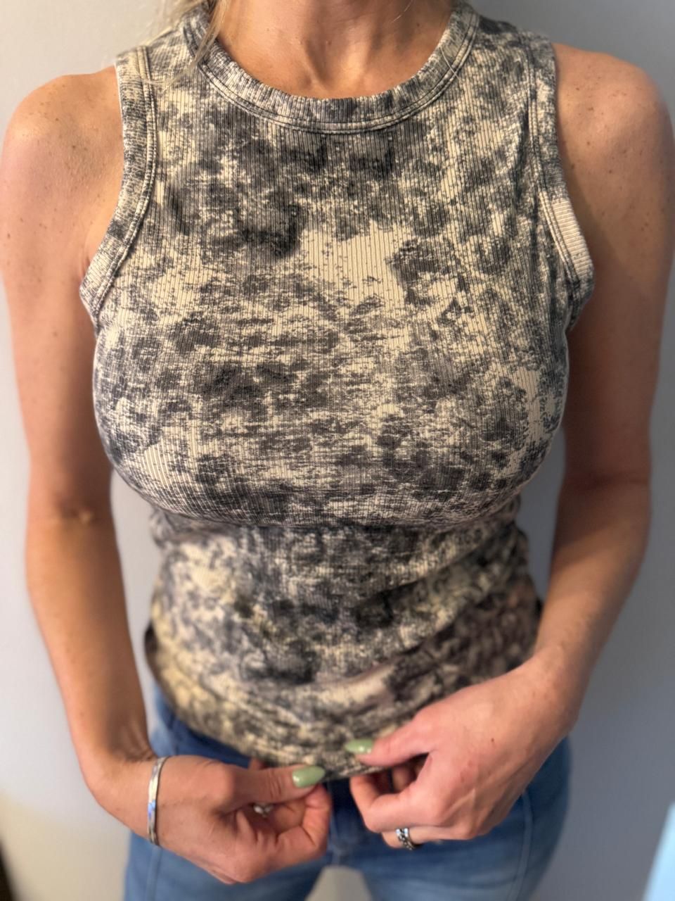 Mujer con una camiseta de tirantes acanalada con estampado tie-dye. Tira del bajo de la camisa.