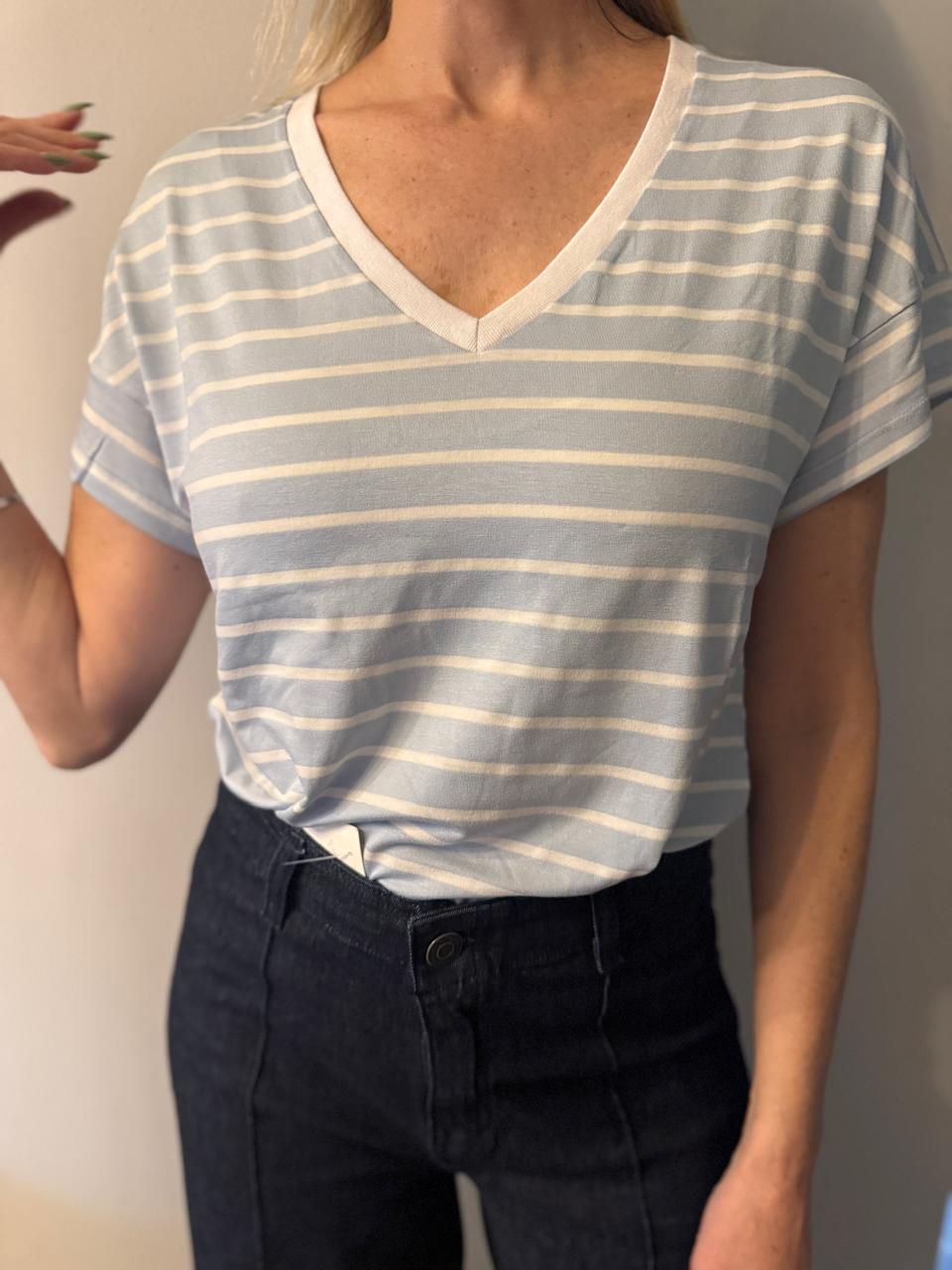 Mujer vestida con una camisa de cuello en V a rayas azul claro y blanco y jeans azul oscuro.