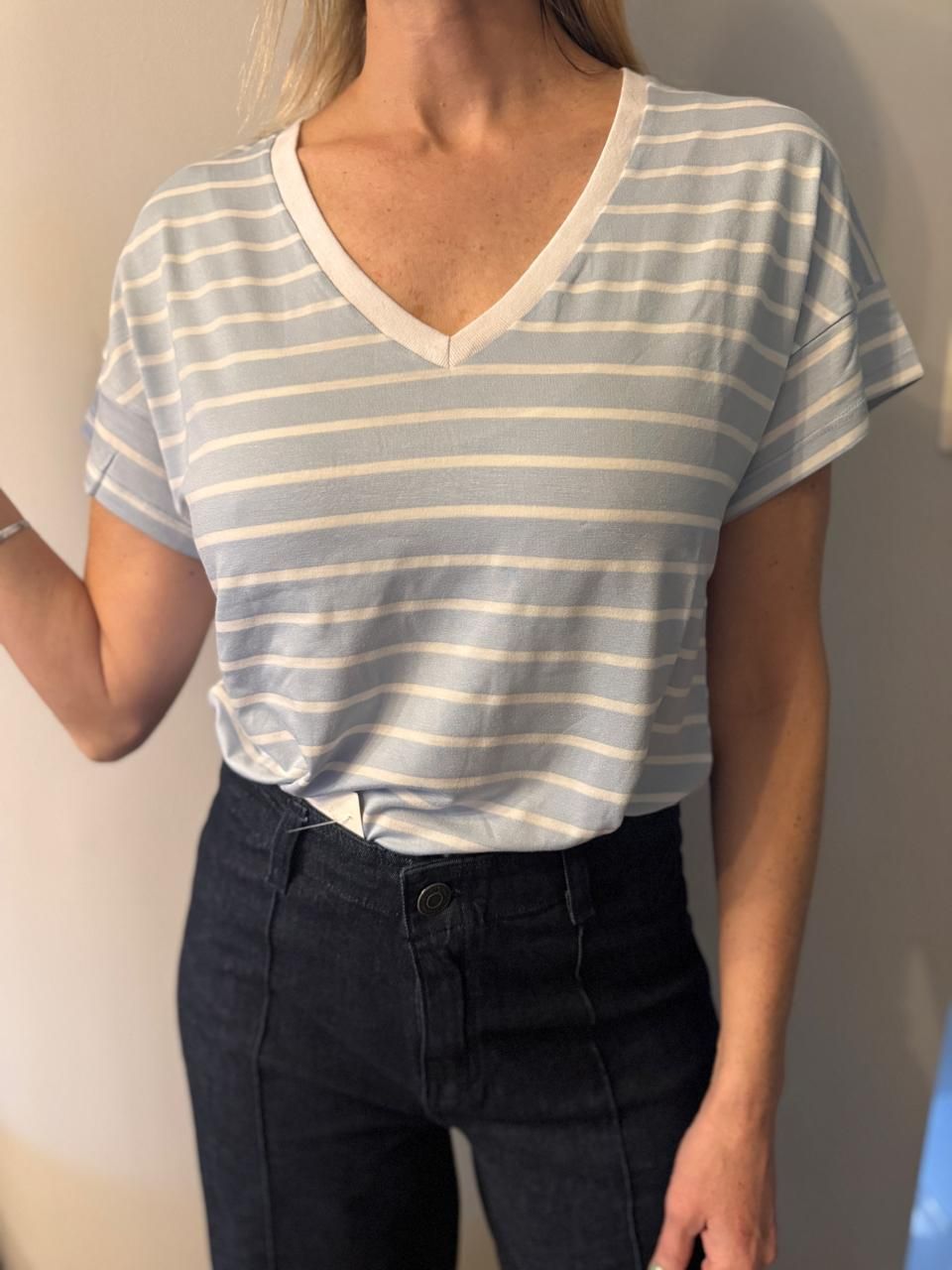 Mujer vestida con una camisa de cuello en V a rayas azul claro y blanco y jeans azul oscuro.