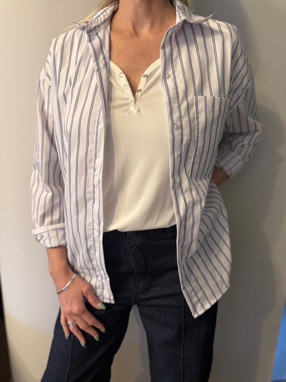 Mujer con camisa de rayas blancas y azules, top blanco y jeans oscuros.