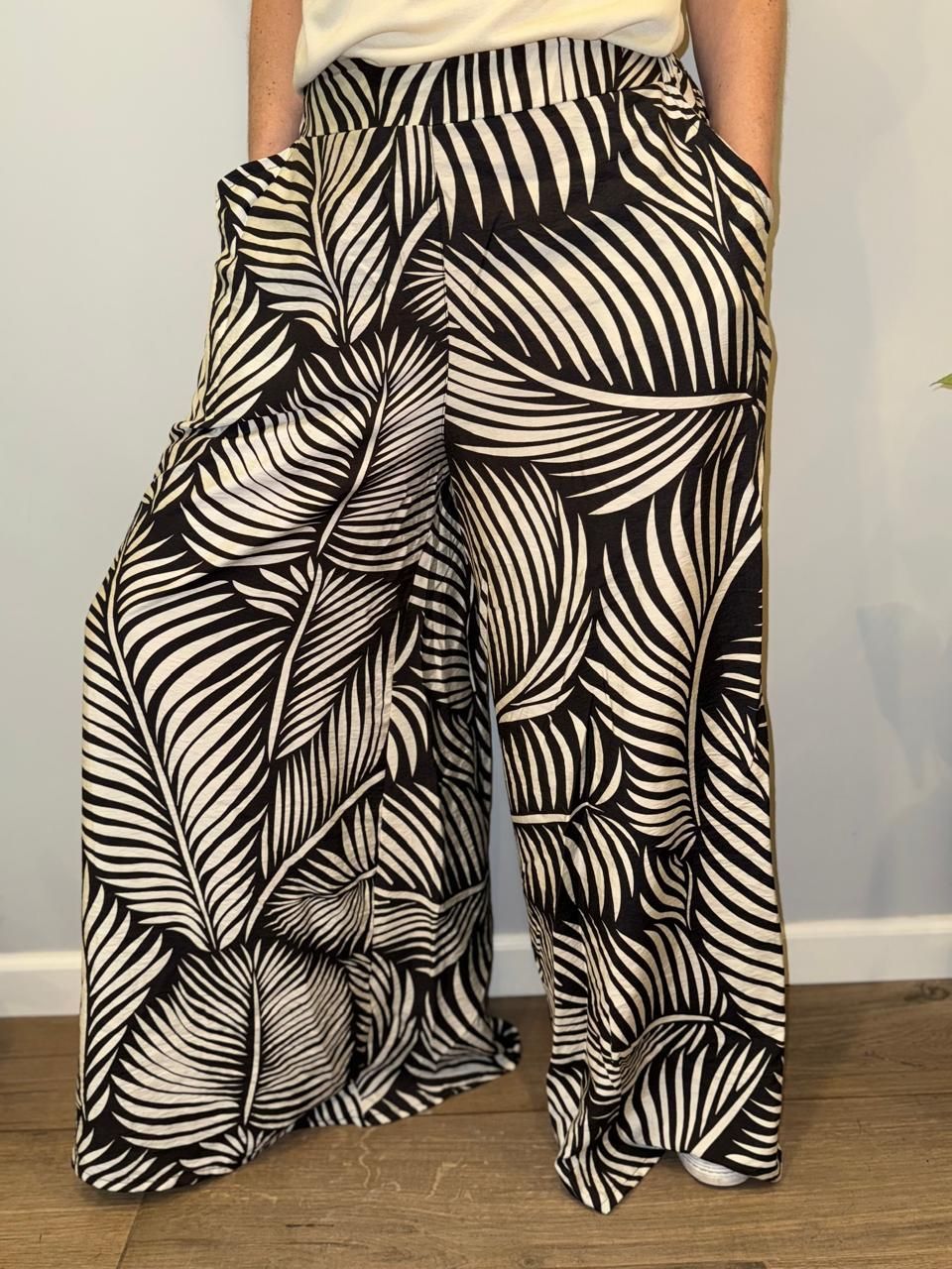 Pantalones anchos con estampado de hojas en blanco y negro. Una persona los lleva con las manos en los bolsillos.