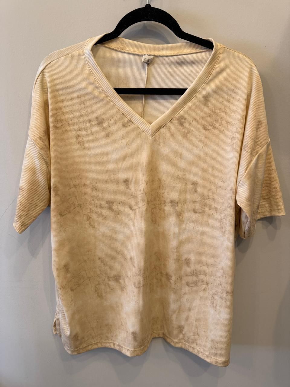 Top de manga corta con escote en V y estampado blanco y gris colgado en una percha negra.