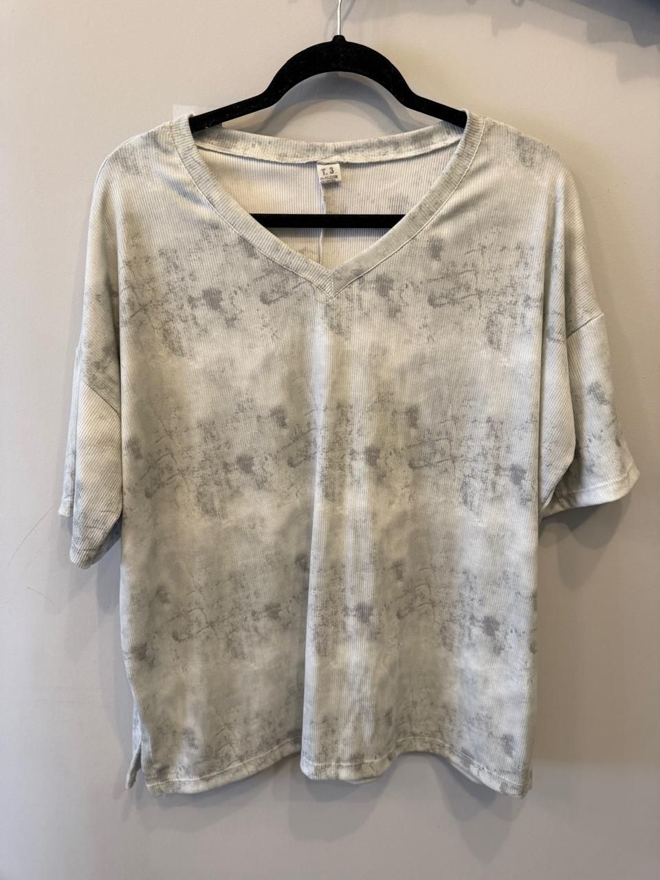 Top de manga corta con escote en V y estampado blanco y gris colgado en una percha negra.